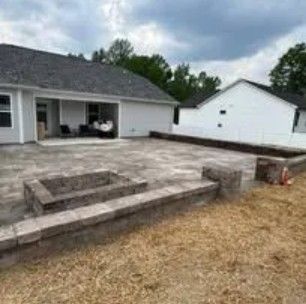 Backyard patio with fire pit, bordering retaining walls, and a white house under a cloudy sky.