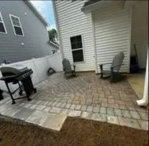 Backyard patio with brick pavers, two chairs, grill, and house siding.