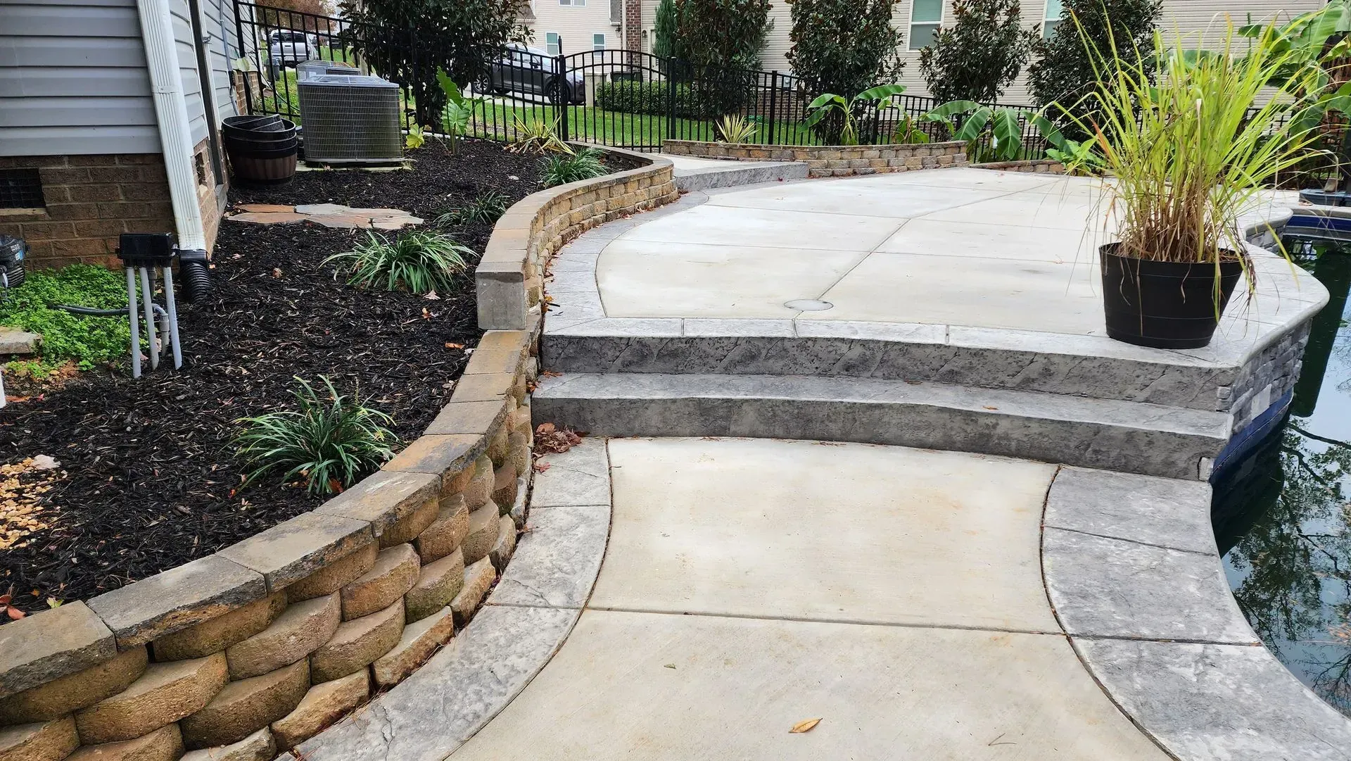 Stone patio with retaining wall, steps, and pool edge, with plants and dark mulch.