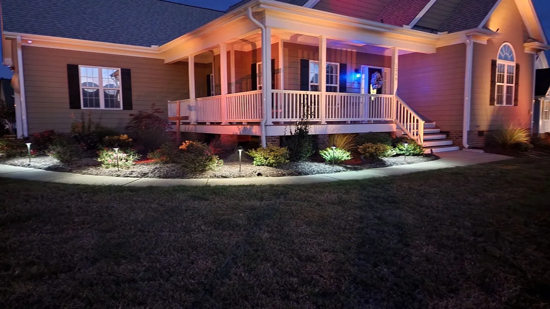 Nighttime shot of a house with illuminated porch and landscape lighting.
