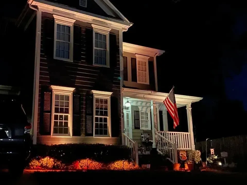 Two-story house with an American flag on the porch; lit with orange lights at night.