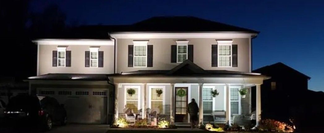 Lit up two-story house at dusk. Lights illuminate the house's exterior and porch.