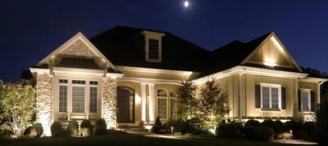 Lit house at night, illuminated by spotlights, with a dark blue sky and the moon visible.