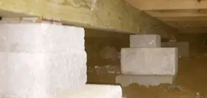 Crawl space with cinder block supports under wooden beams, some in standing water.