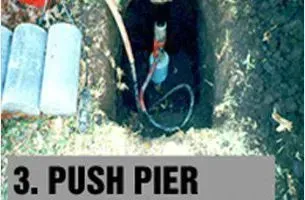 Worker installing push pier in a trench, alongside concrete cylinders.