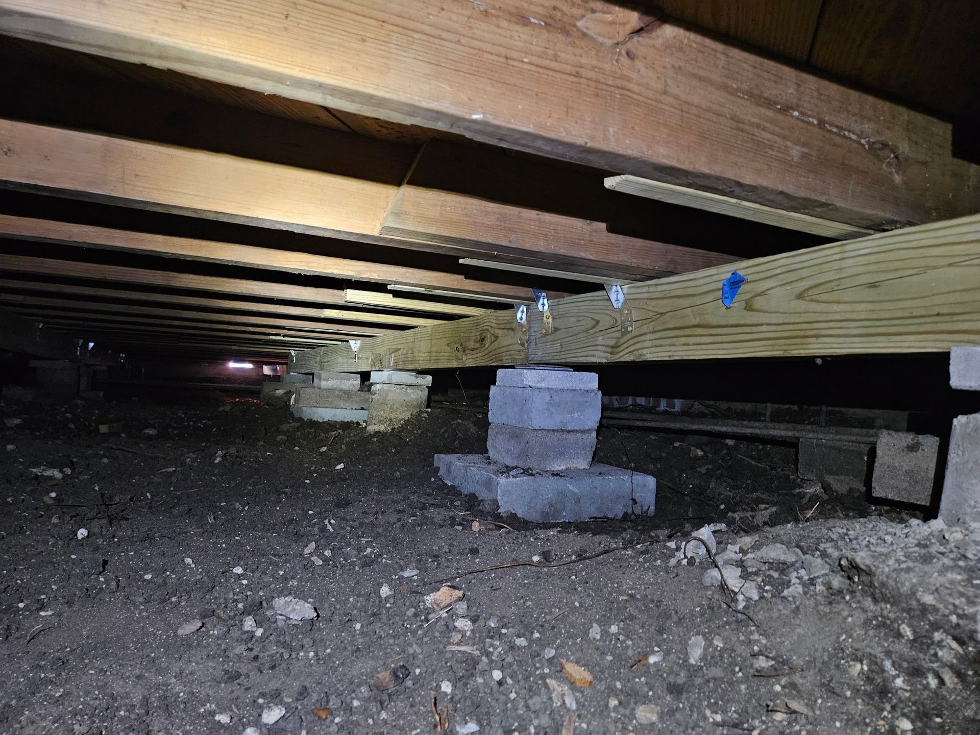 Support beams made of wood and cinder blocks in a crawl space under a building.