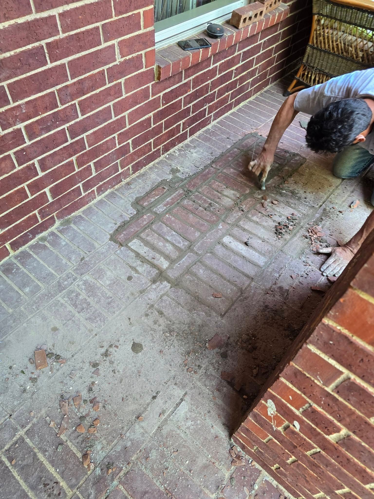 Person cleaning brick patio with a brush. Brick walls and herringbone pattern bricks.