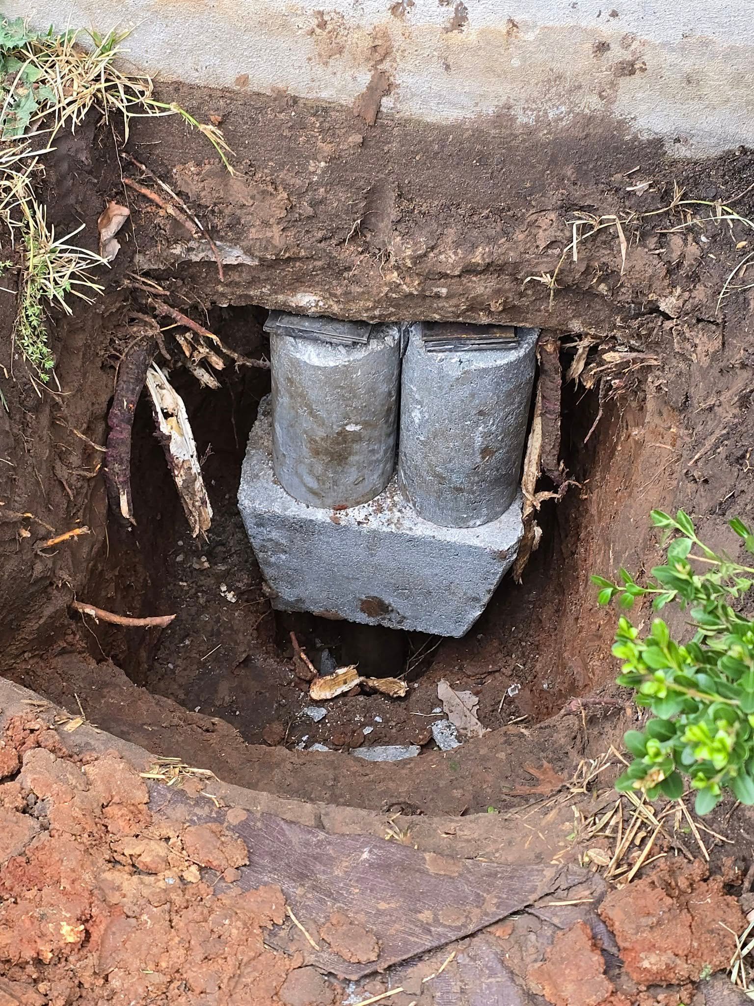 A hole dug into the ground revealing a concrete structure with two cylindrical columns.