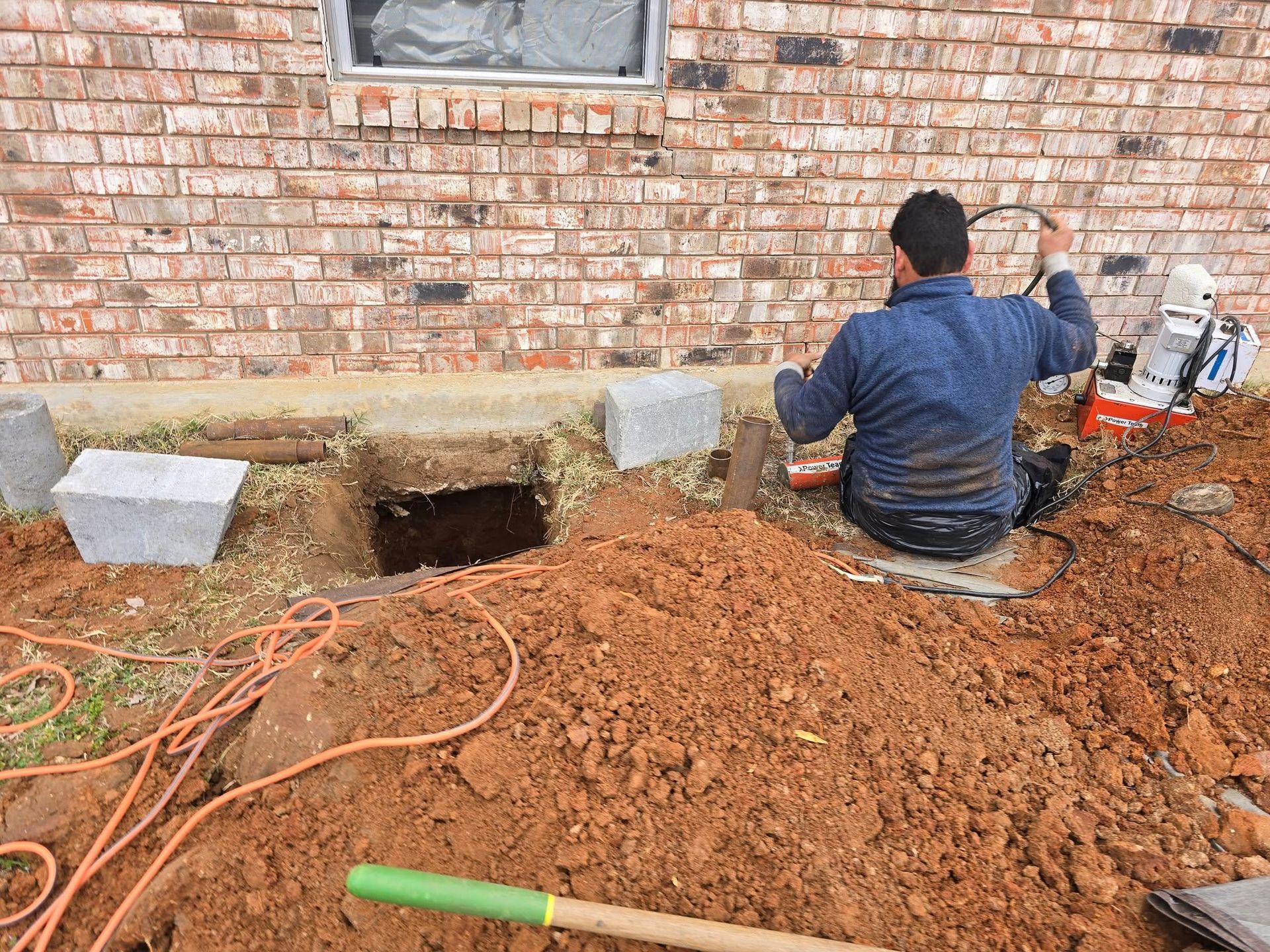 Man digging near a brick building; concrete blocks and soil visible.