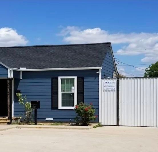 Blue house with black shutters, white window, and a white fence against a blue sky.