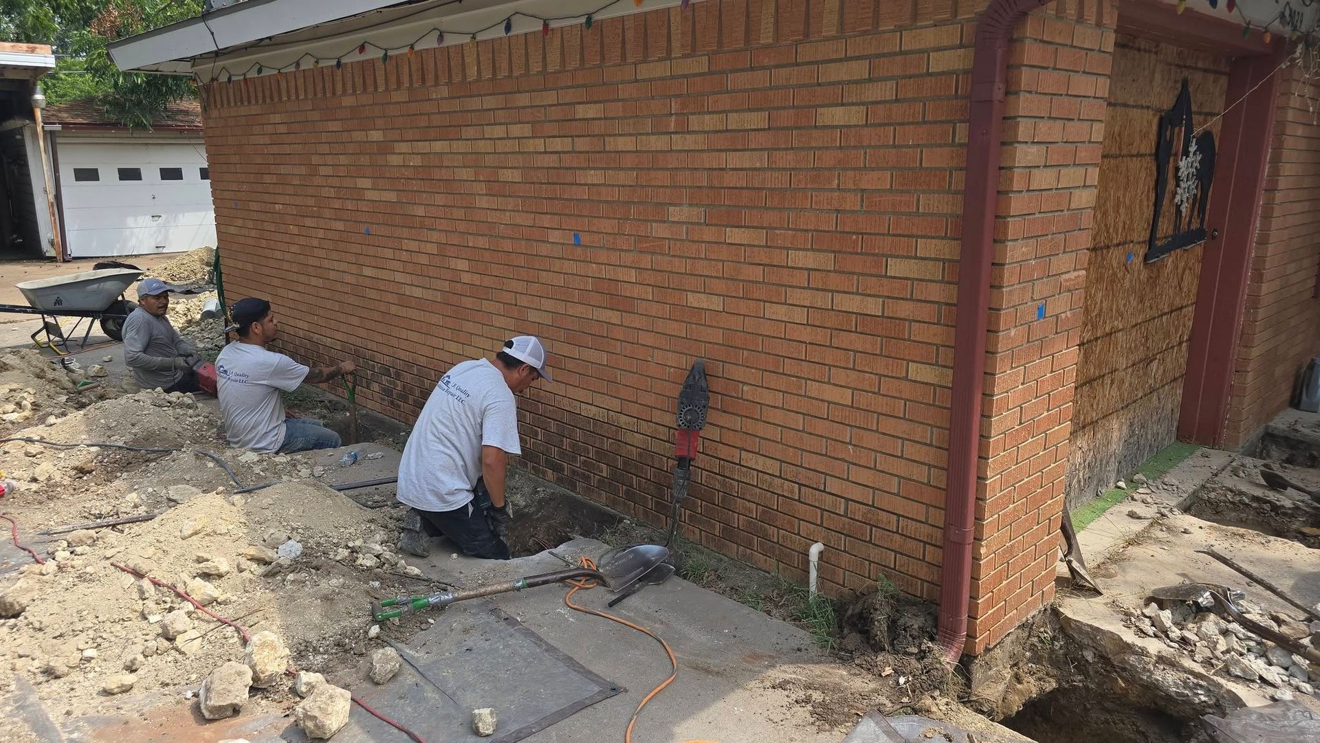 Workers excavating around a brick building's foundation. Dirt piles surround them.