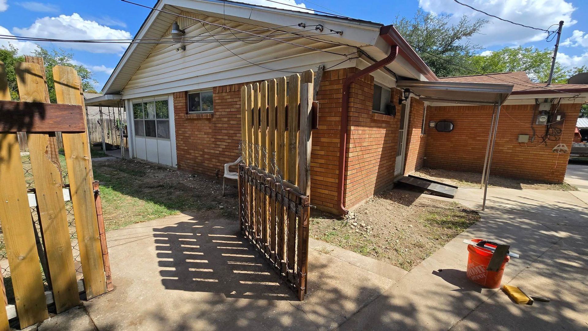 Small brick house with wooden gate and fence; sunny day.