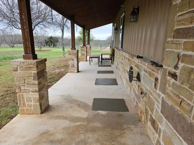 Covered porch with stone columns and walls, concrete floor, outdoor furniture.