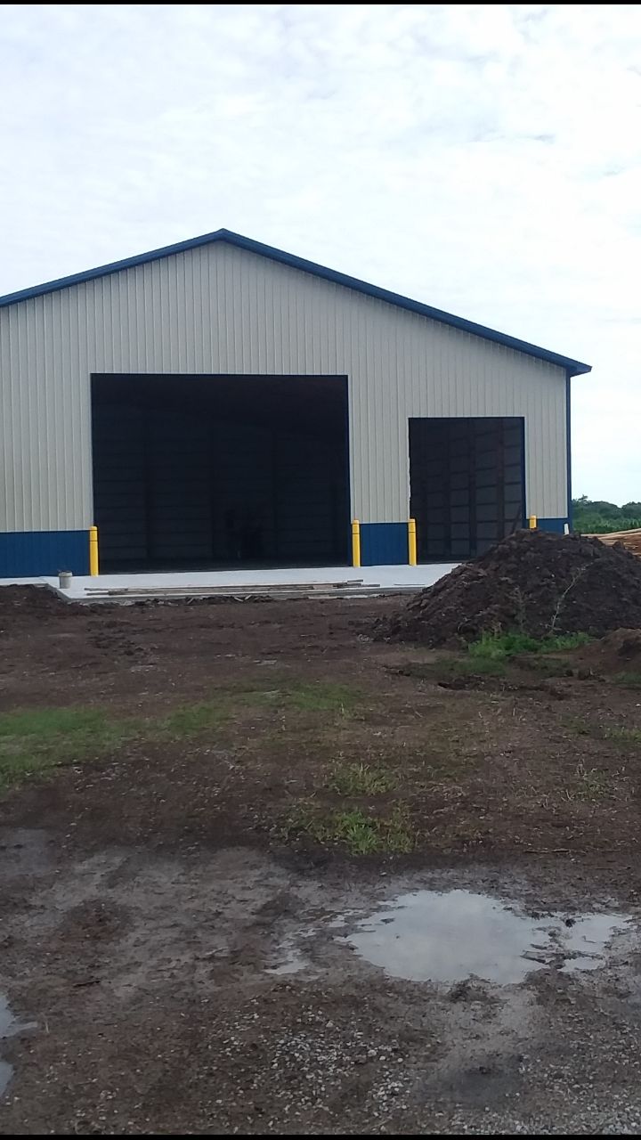 A large metal building with two large doors is sitting in the middle of a dirt field