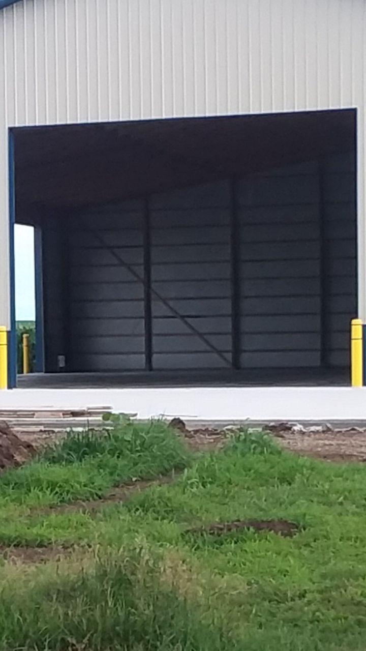 A large metal building with a large sliding door is sitting in the middle of a grassy field