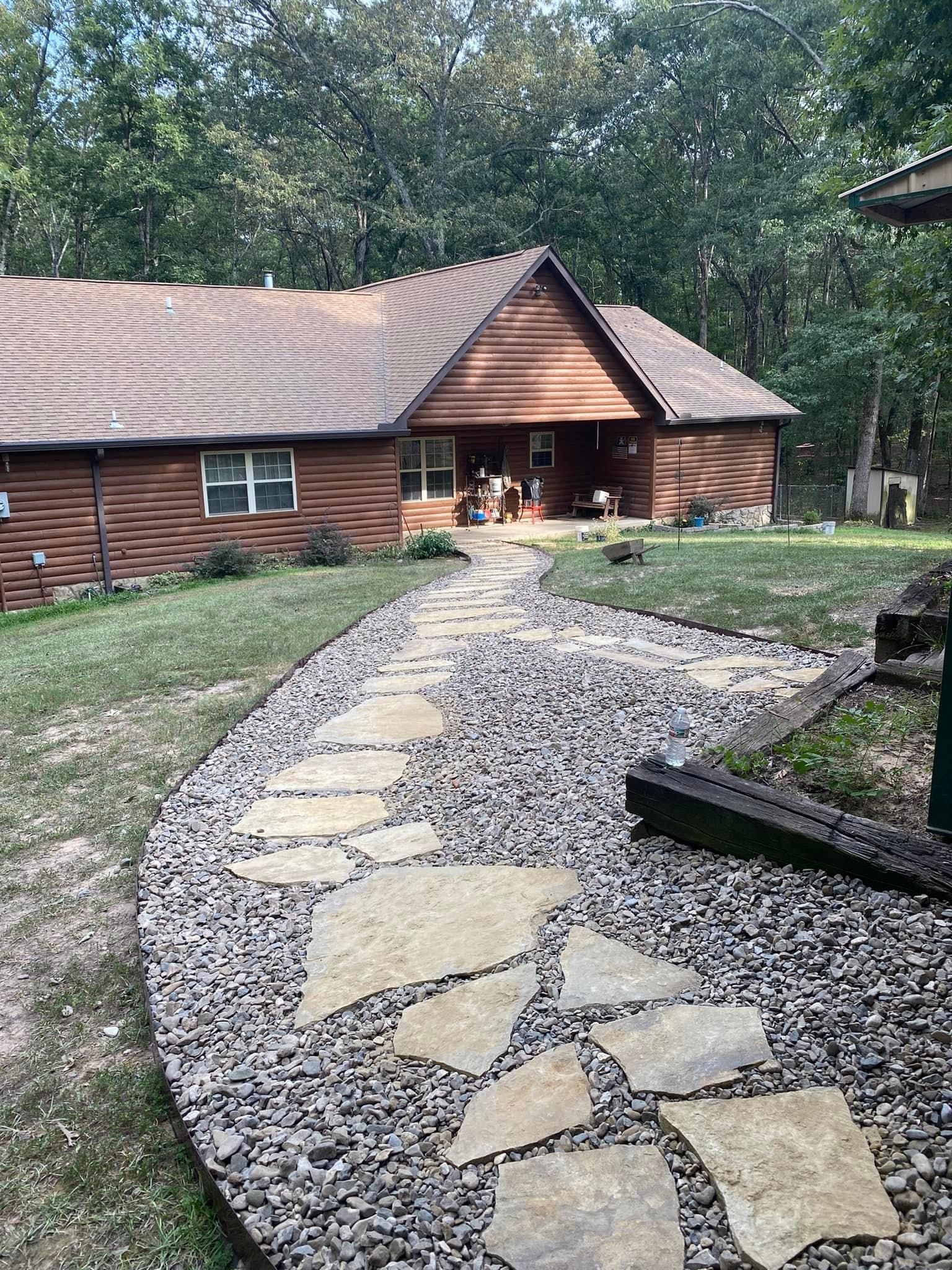 Stone path leads to a wooden house with a porch, surrounded by grass and trees.