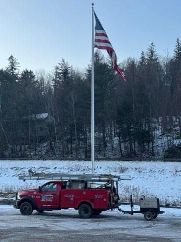 Red truck with trailer parked by a tall American flagpole in a snowy roadside setting