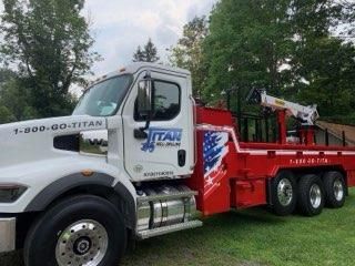 White tow truck with red bed and ITAN logo parked outdoors on grass near trees