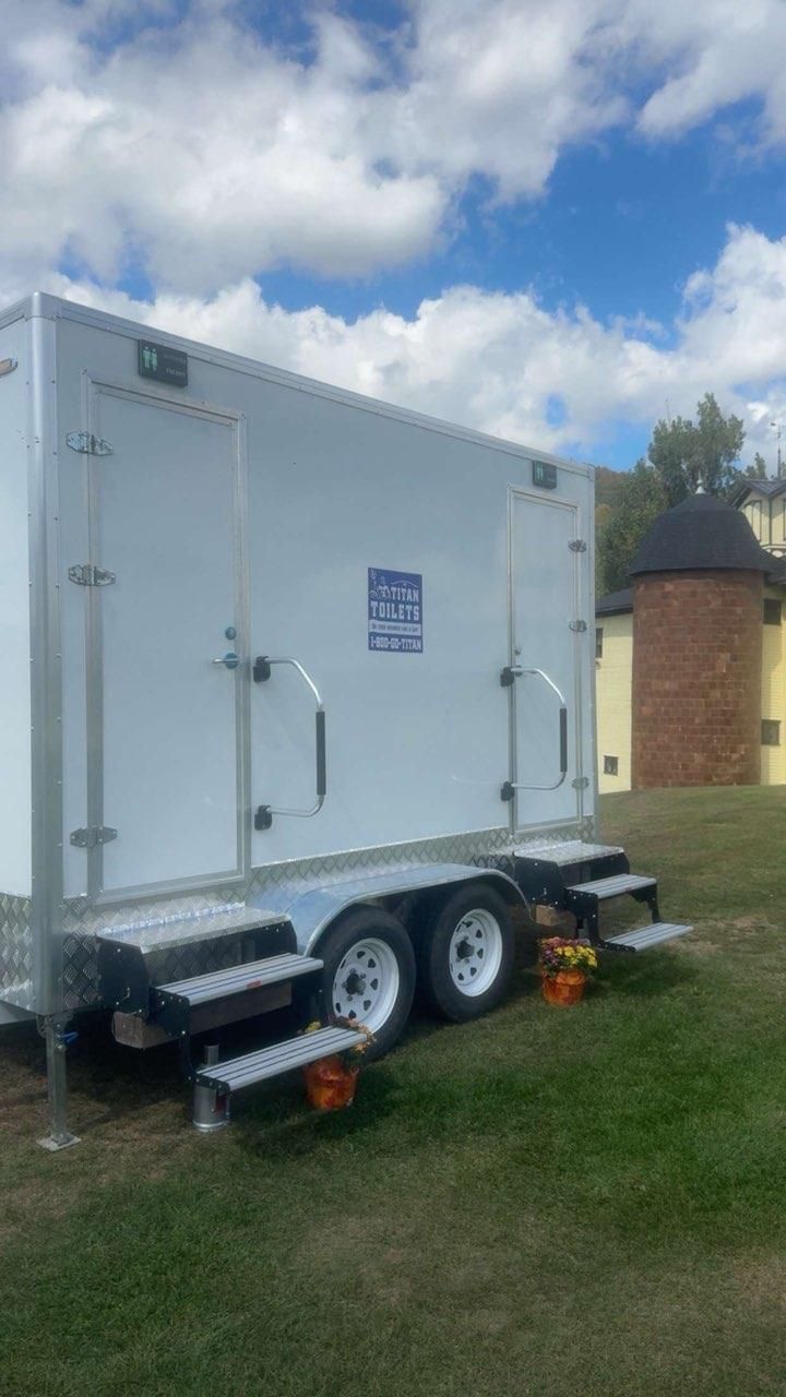 White enclosed cargo trailer parked on grass under a blue sky, with dual axles and a black front cover