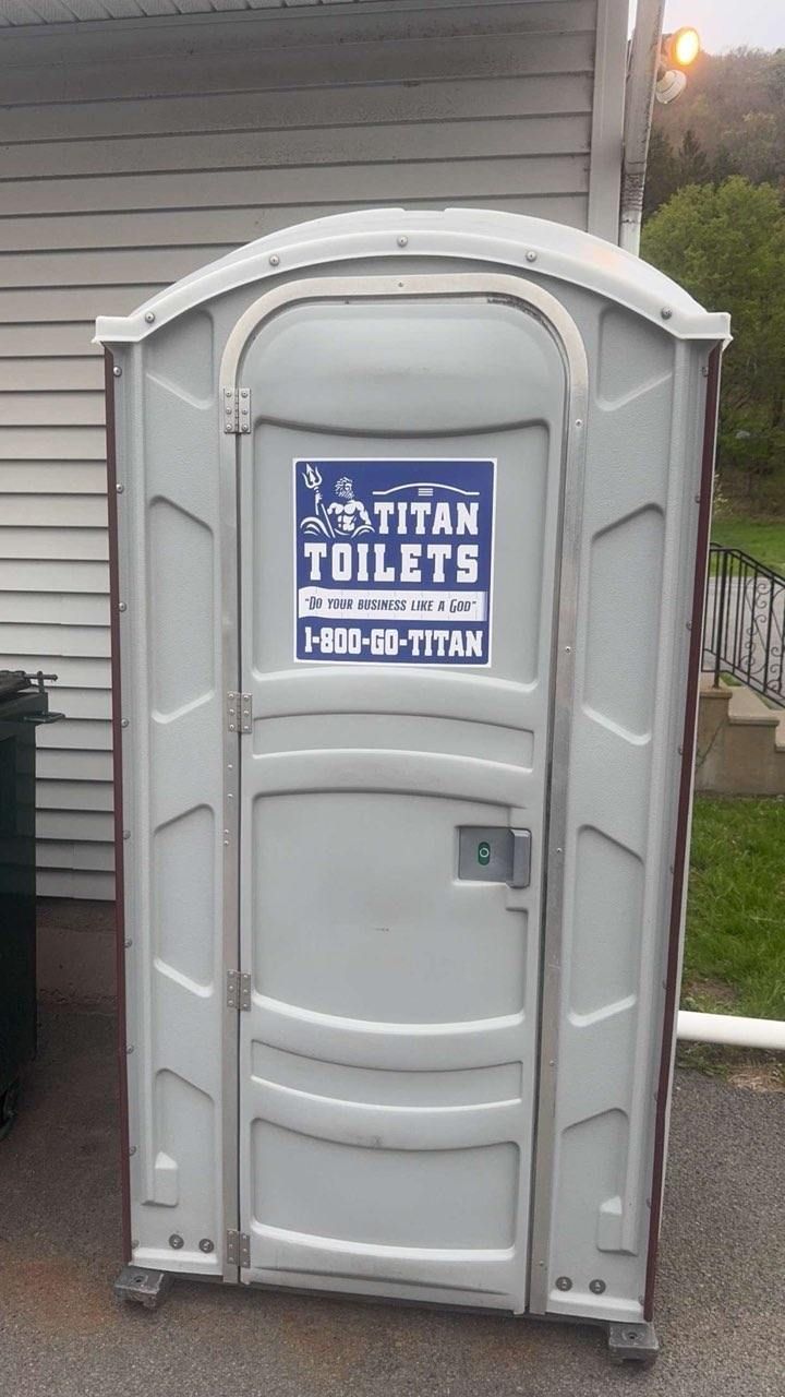 Gray portable toilet with a blue “Ahern Toilets” sign on the door outdoors