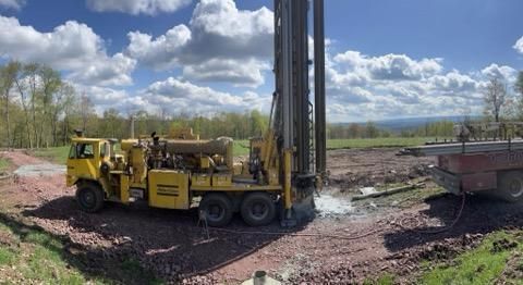 Yellow drilling rig on muddy construction site under cloudy sky, with a trailer nearby