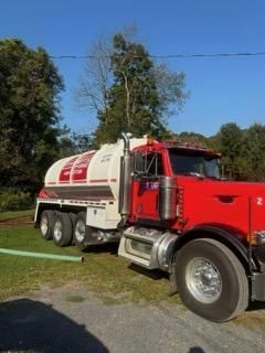Red truck with white tanker trailer parked on a grassy roadside under a clear blue sky