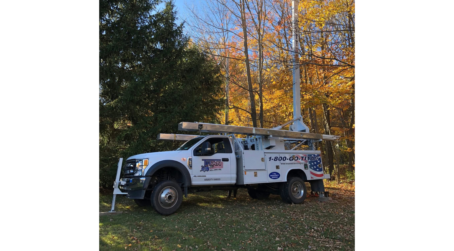 White utility truck parked on grass beside autumn trees and a yellow house