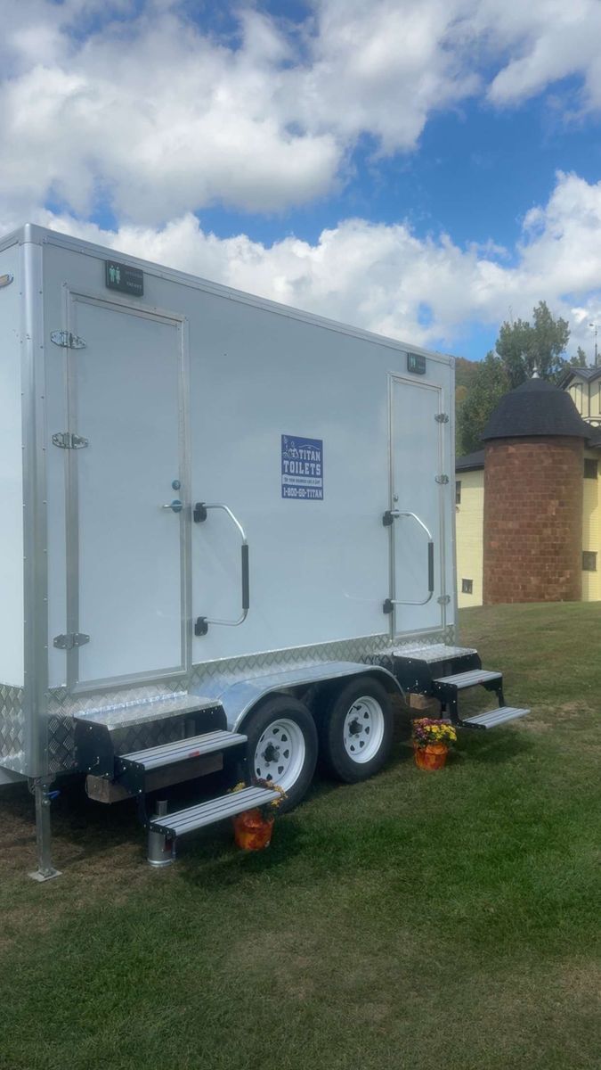 White portable restroom trailer with steps, on grass, blue sky background.