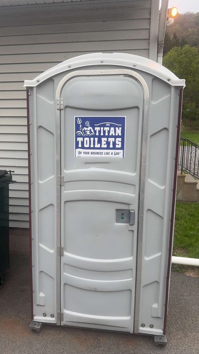 Gray portable toilet with a “Weston Toilets” sign on the door outdoors