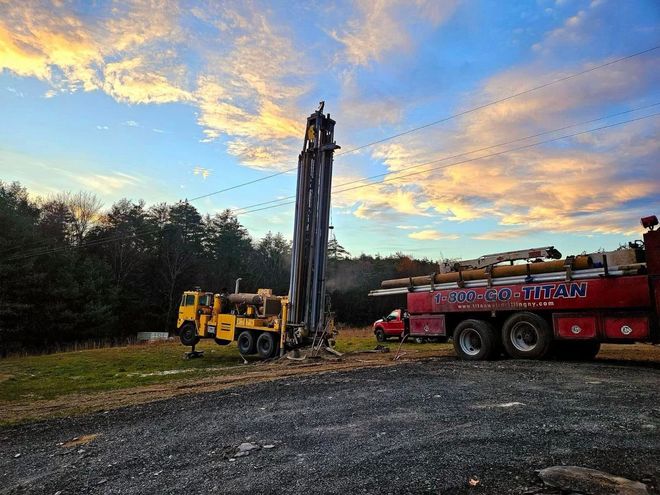 Yellow drilling rig and red truck at a construction site under a cloudy sunset sky