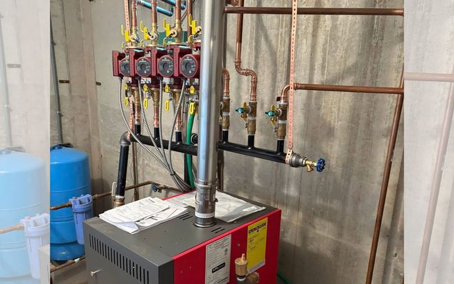 Industrial boiler room with red boiler, vertical pipes, and blue tanks against concrete walls