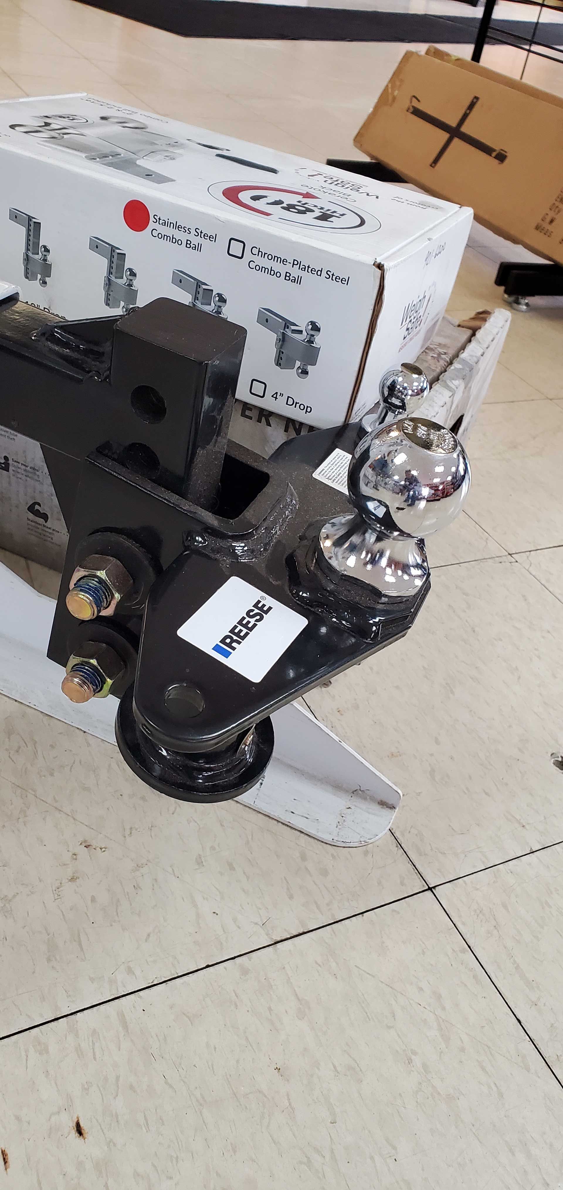 Black-and-silver mechanical device on a tiled floor beside a cardboard box and marker label.