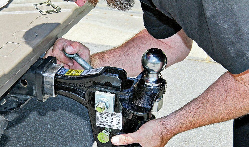 Hands attaching a trailer hitch to a vehicle, with a shiny tow ball and safety chain clip.