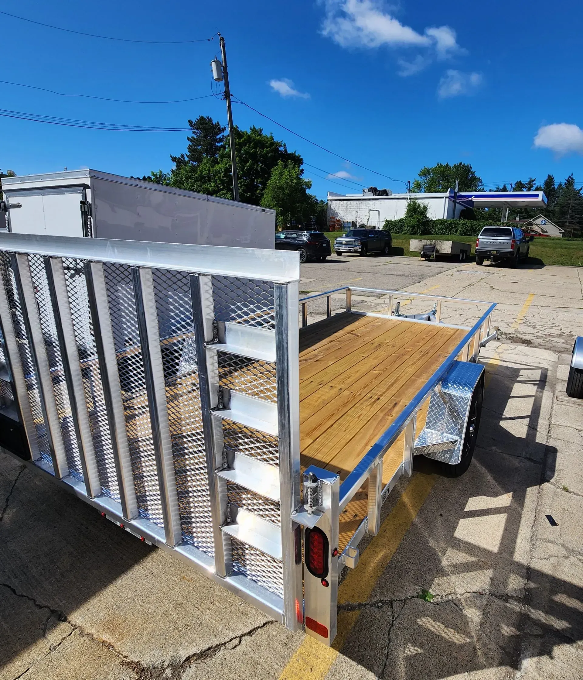 Empty utility trailer with wooden floor parked on a gravel lot under a blue sky