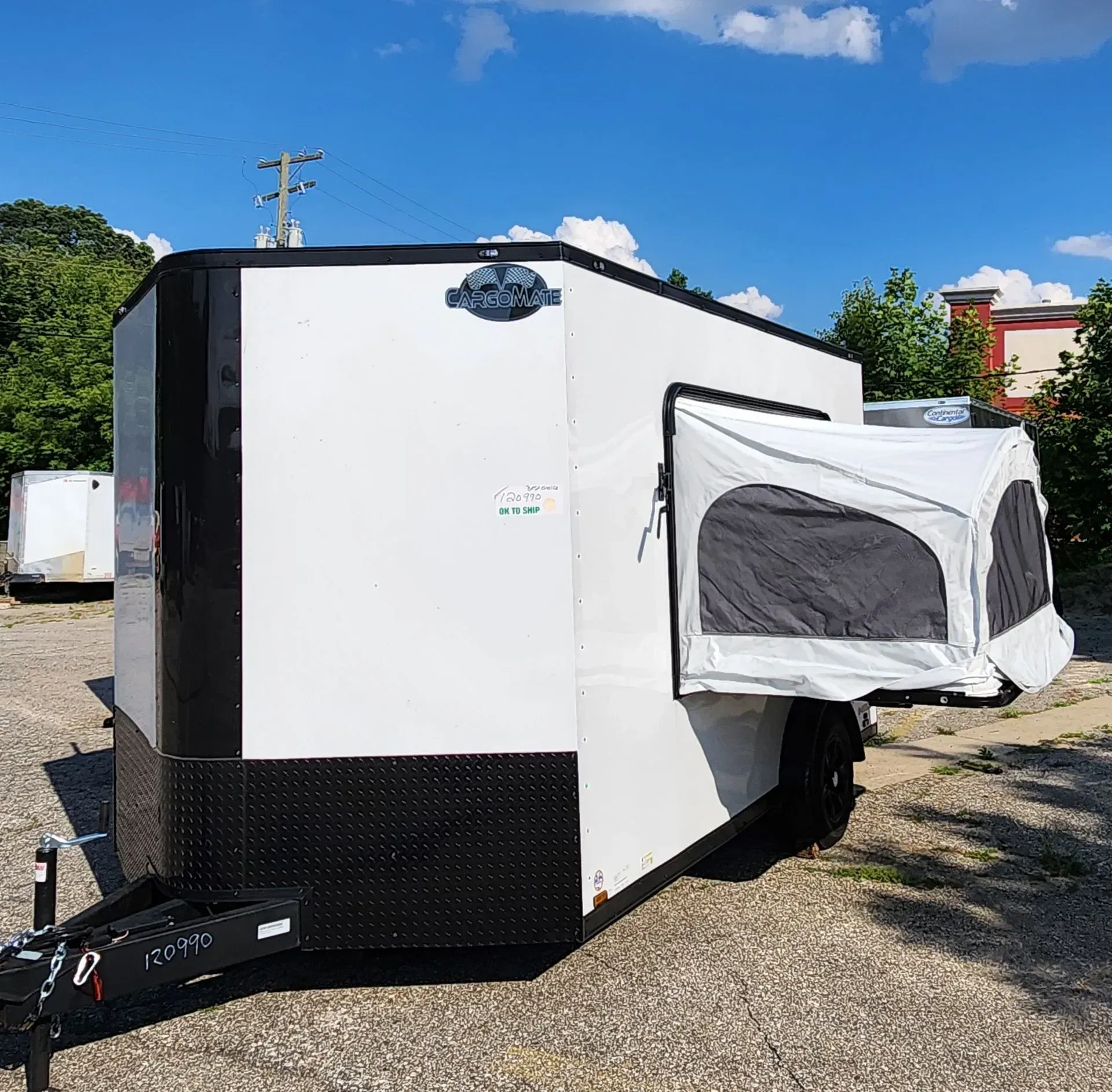 White cargo trailer with extended side pop-out and black trim parked outdoors on a gravel lot under a blue sky