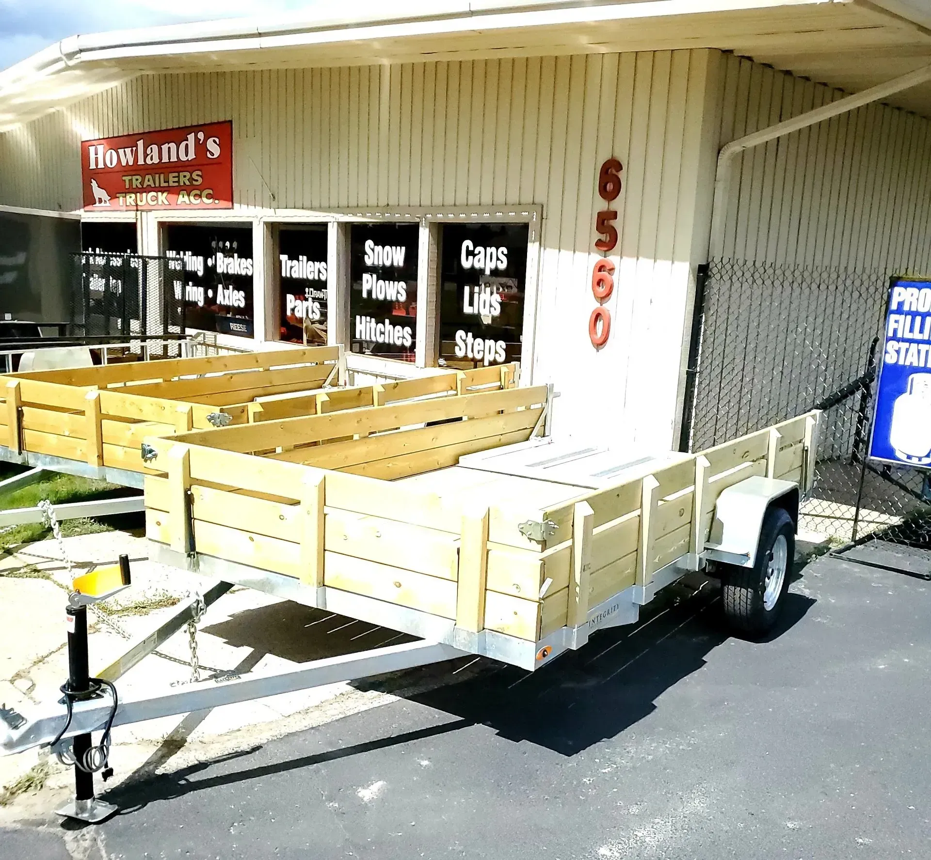 Wooden utility trailer parked outside a farm supply store with red signage and numbered building wall