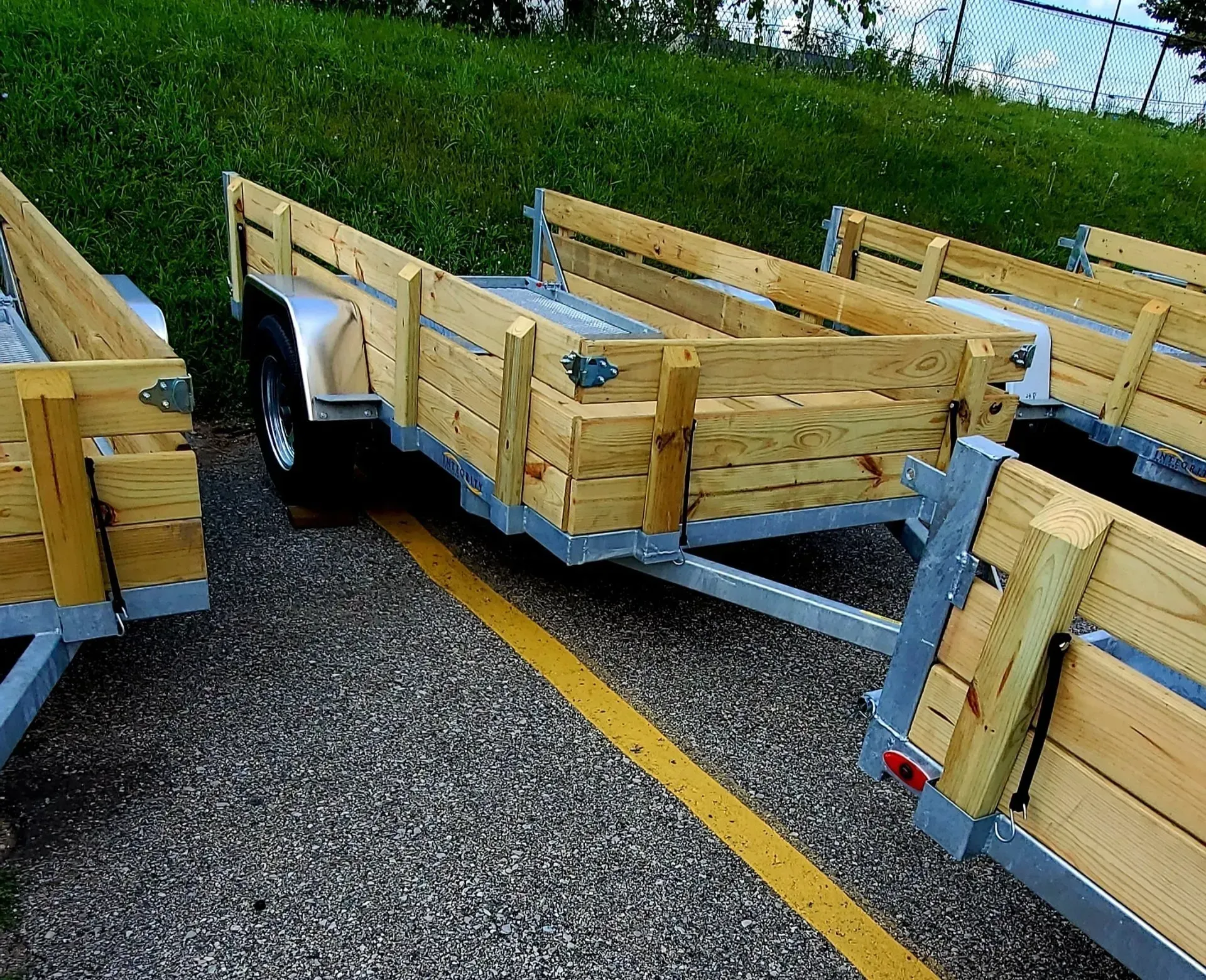 Wooden utility trailers parked on a gravel lot beside grass and water, viewed from above.