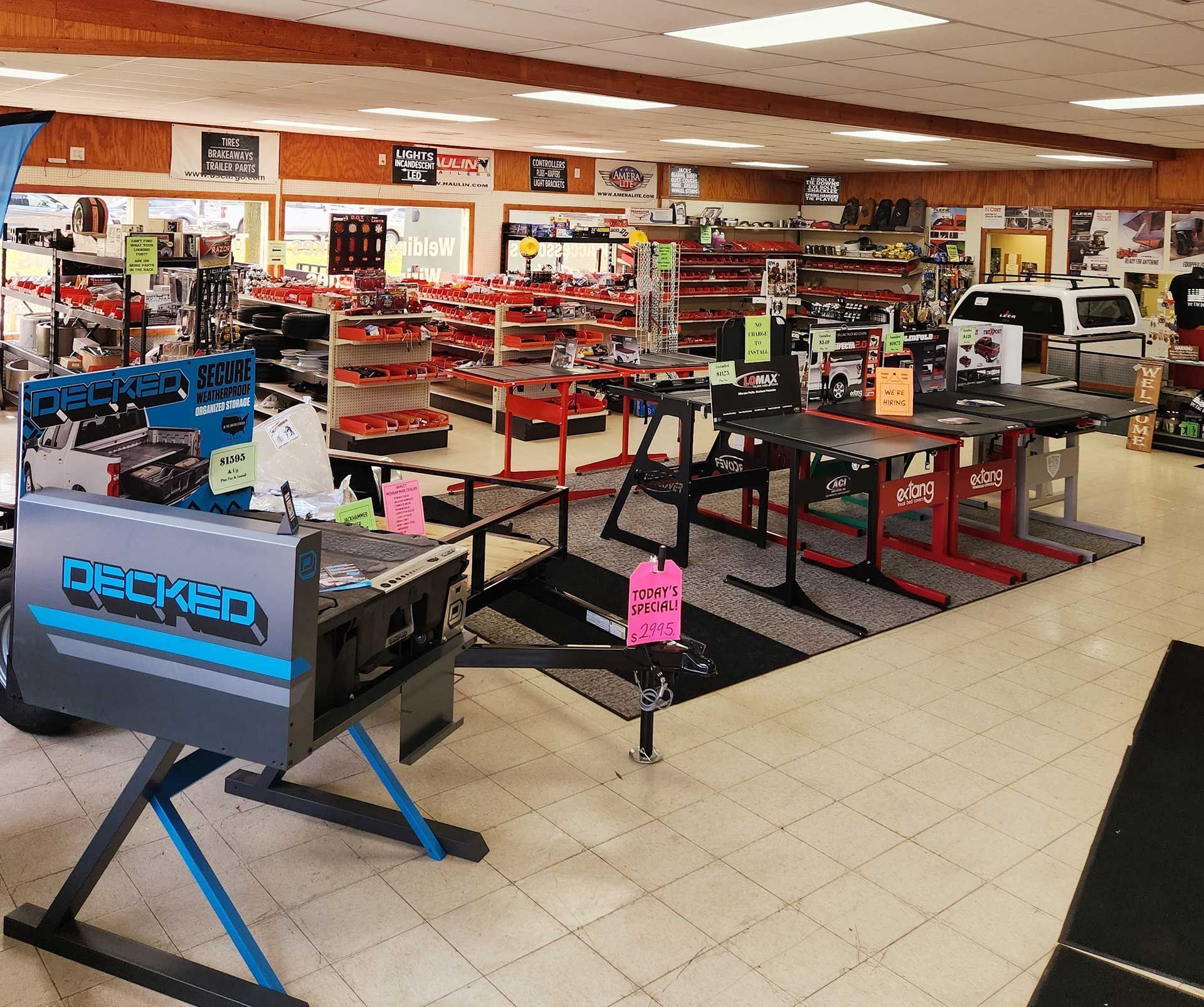 Electronics store interior with display shelves, computer monitors, and gaming chairs on sale.