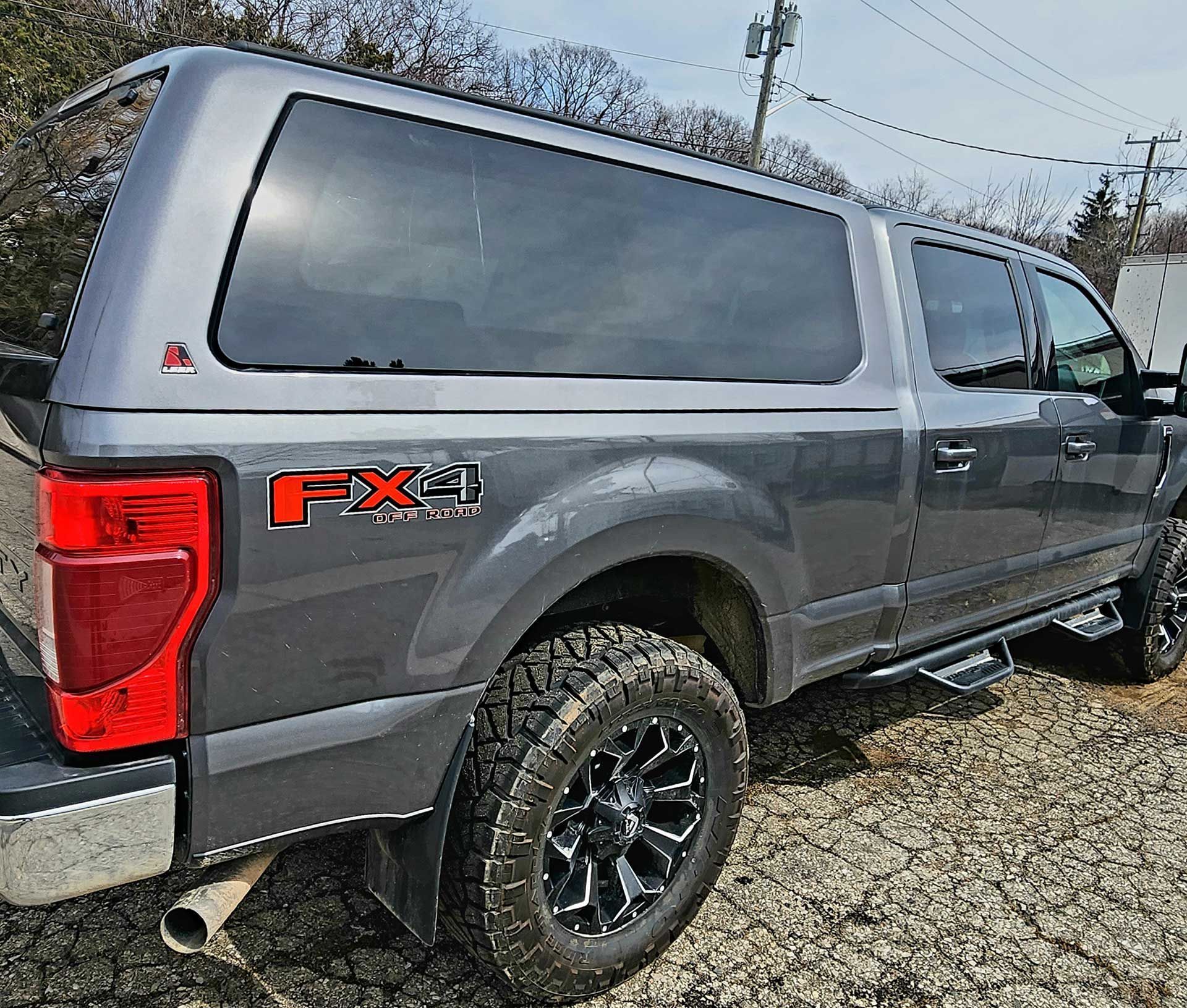 Gray Ford F-150 FX4 pickup with camper shell parked outdoors on gravel