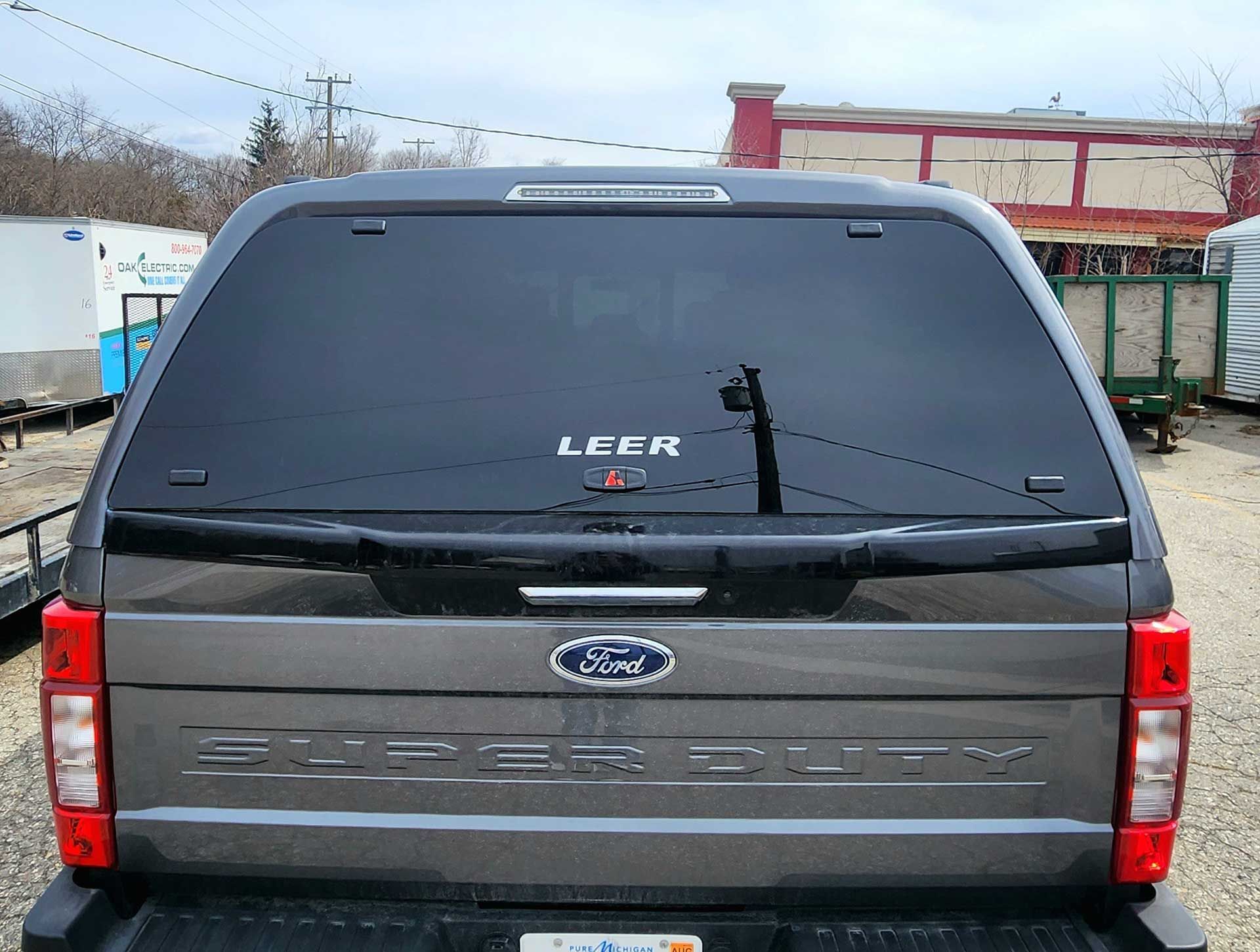 Rear view of a black Ford SUV with a LEER camper shell parked in a lot.