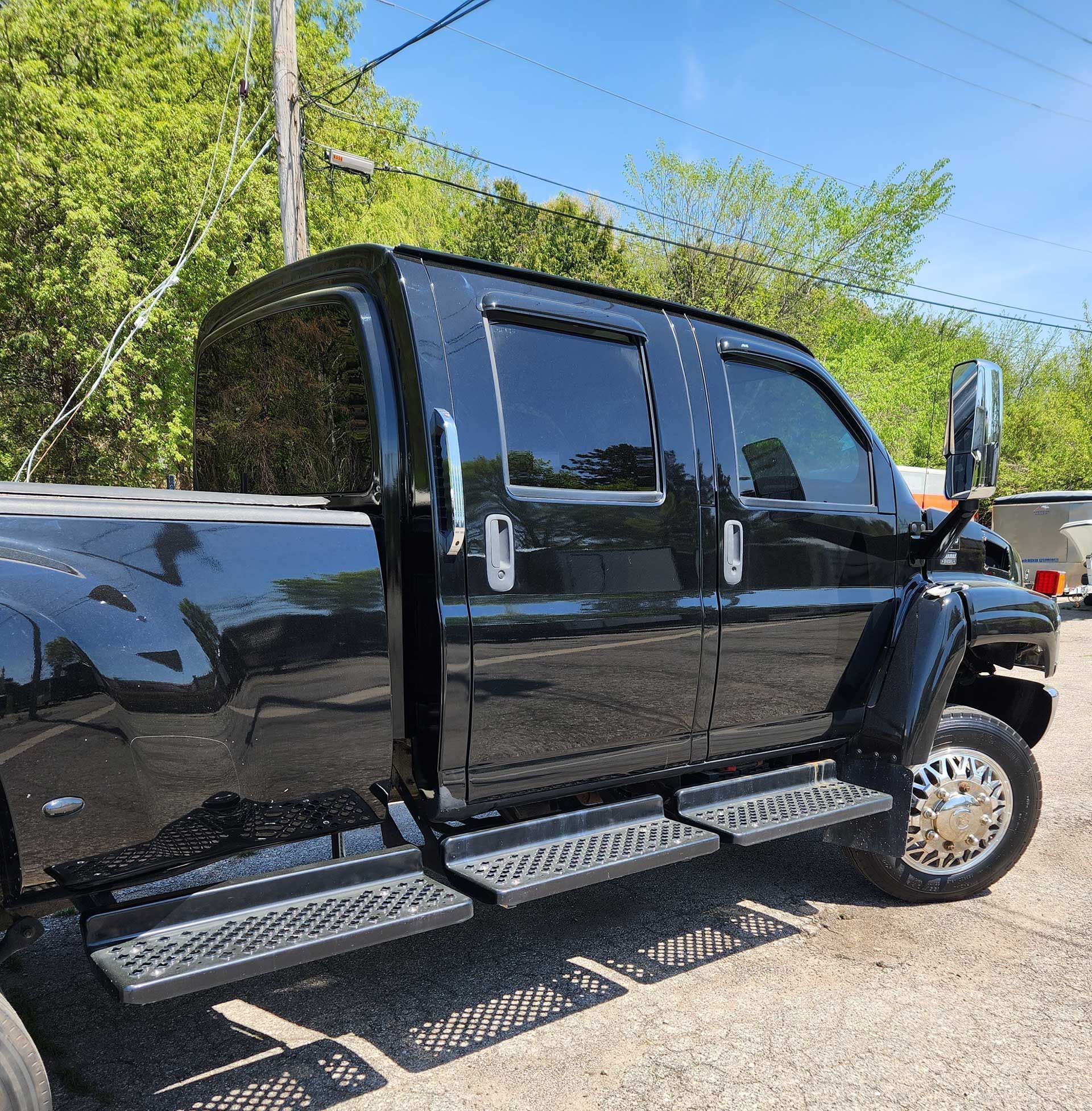 Black lifted crew cab pickup truck parked outdoors in sunlight, side view