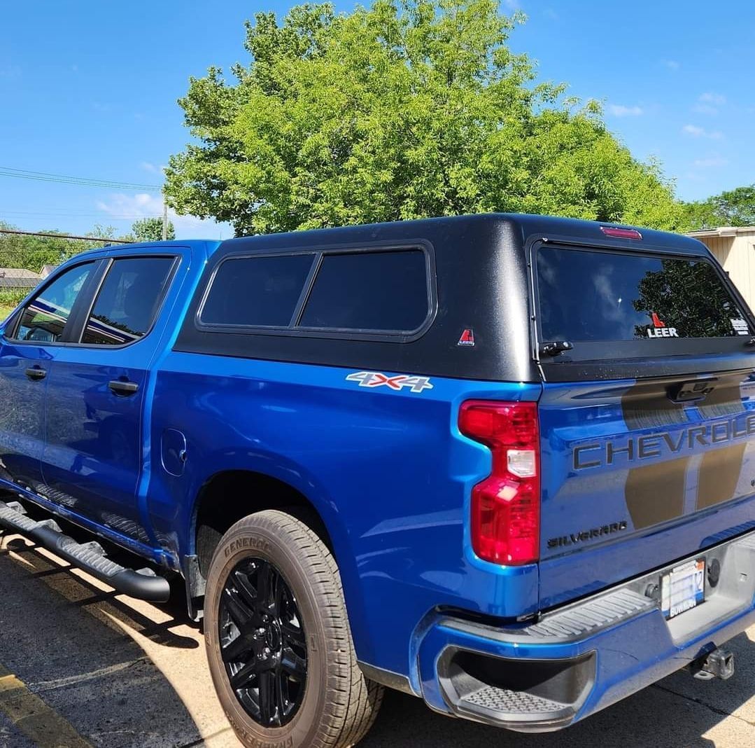 Blue Chevrolet pickup truck with black camper shell parked outdoors on a sunny day