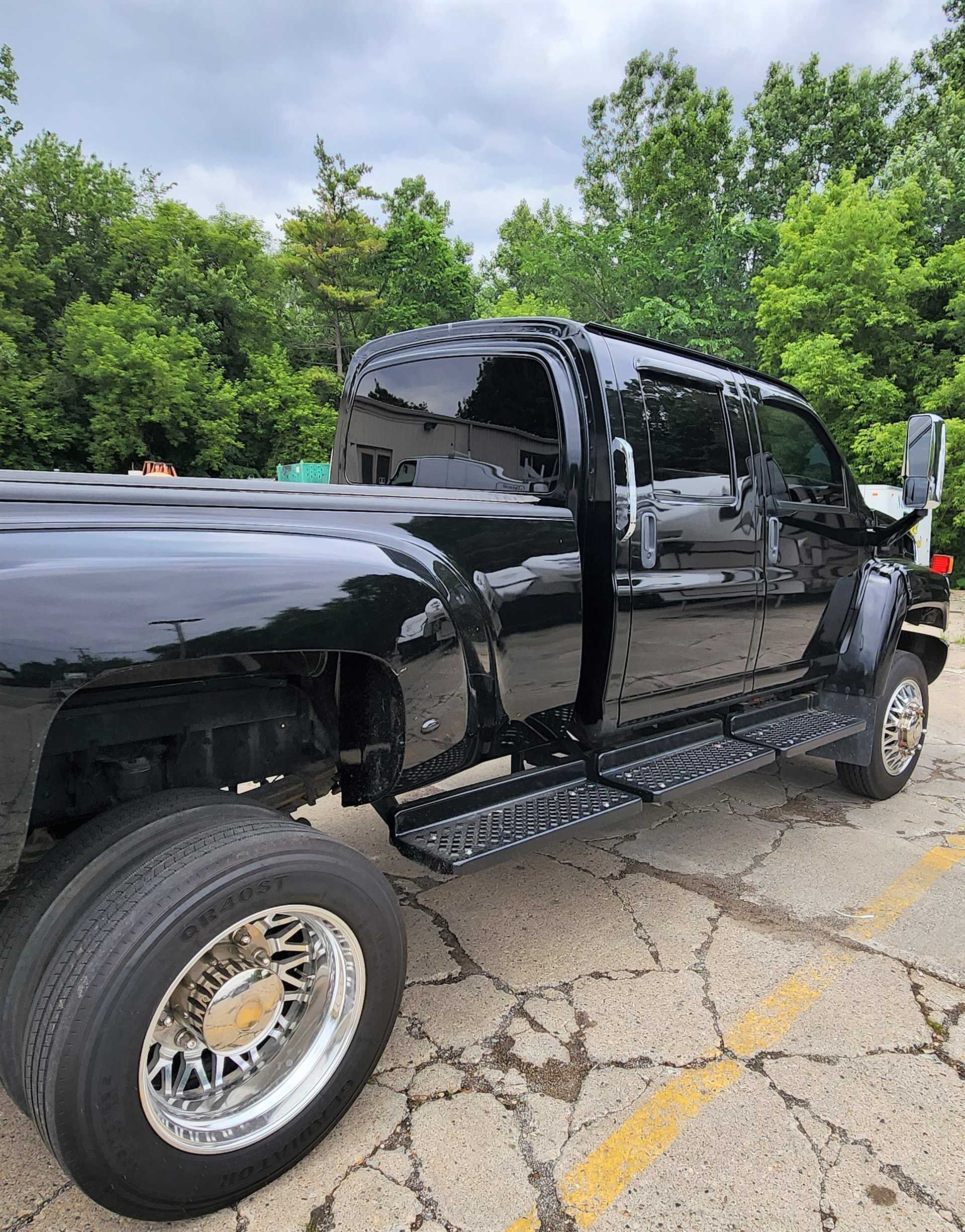 Black lifted pickup truck parked outdoors on a cracked lot beside green trees.