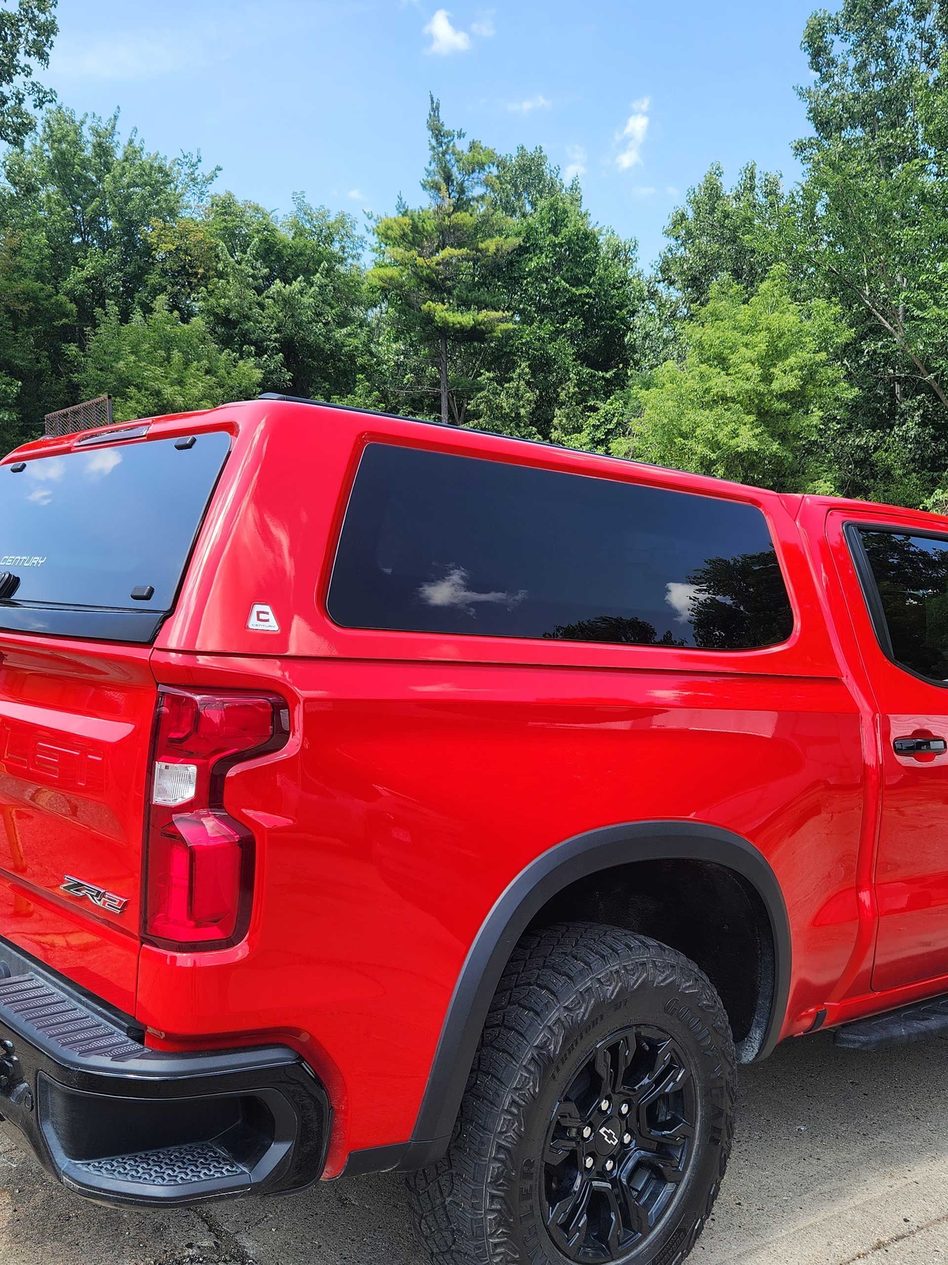 Red pickup truck with black trim parked on gravel near trees under a blue sky