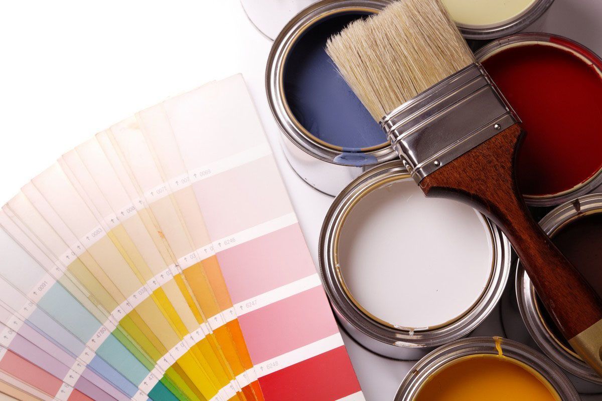 Paint cans with a brush resting on top, placed next to a fan-shaped color swatch deck on a white surface.