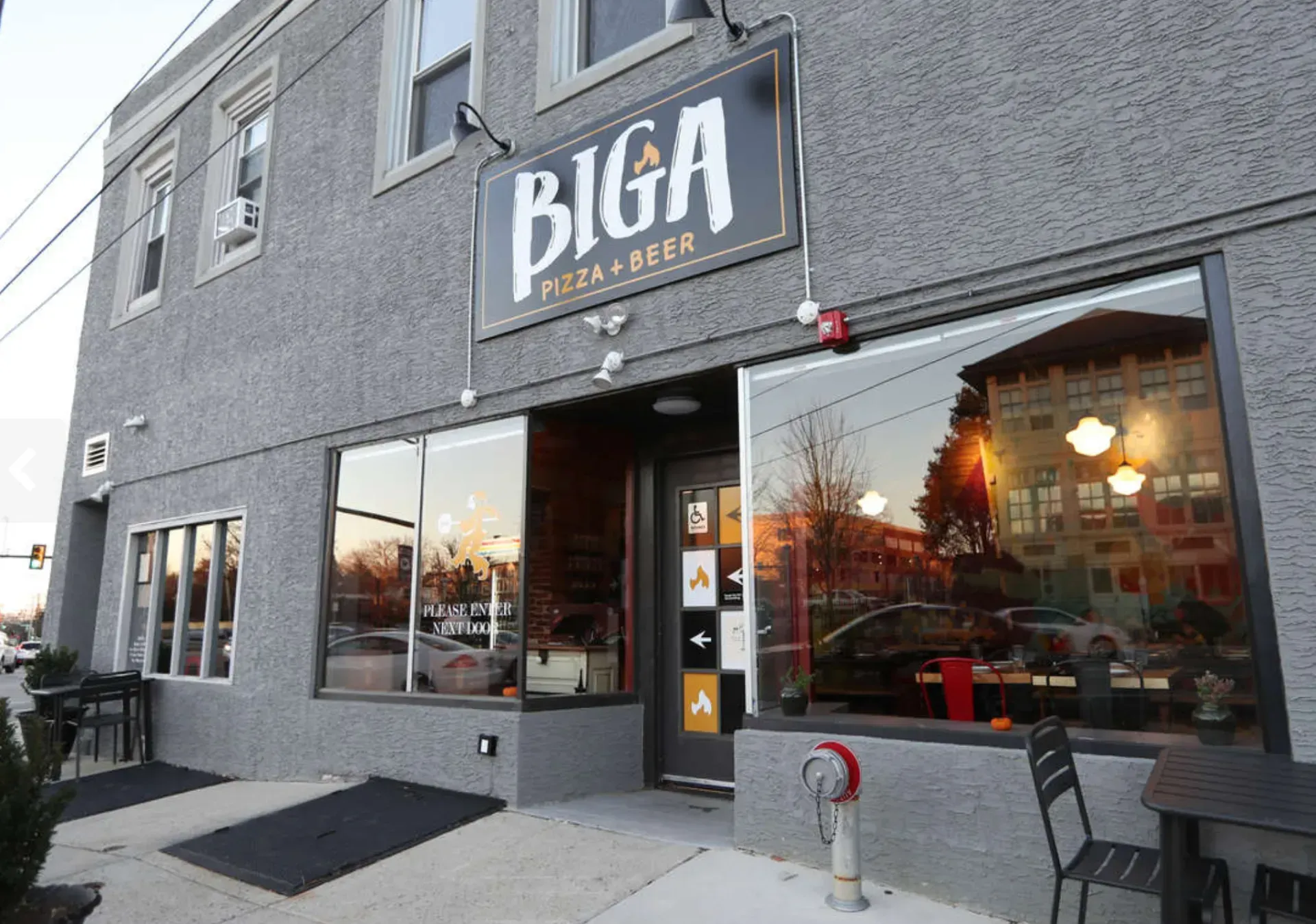 Exterior of BIGA Pizza & Beer restaurant with gray facade and large windows at dusk