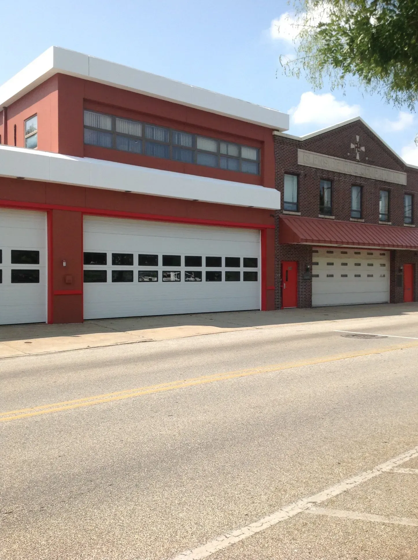 Red fire station with garage bays on a quiet street under a blue sky