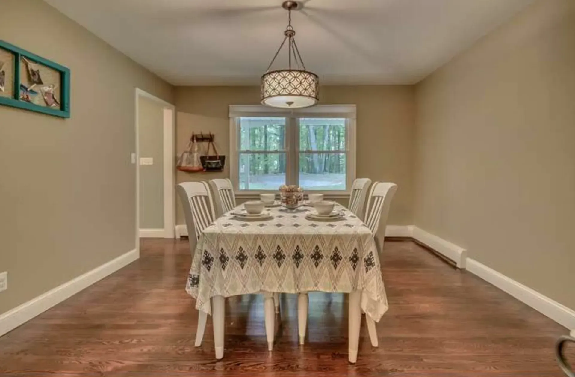 Dining room with a table set for a meal, hardwood floor, beige walls, and a window at the far end.