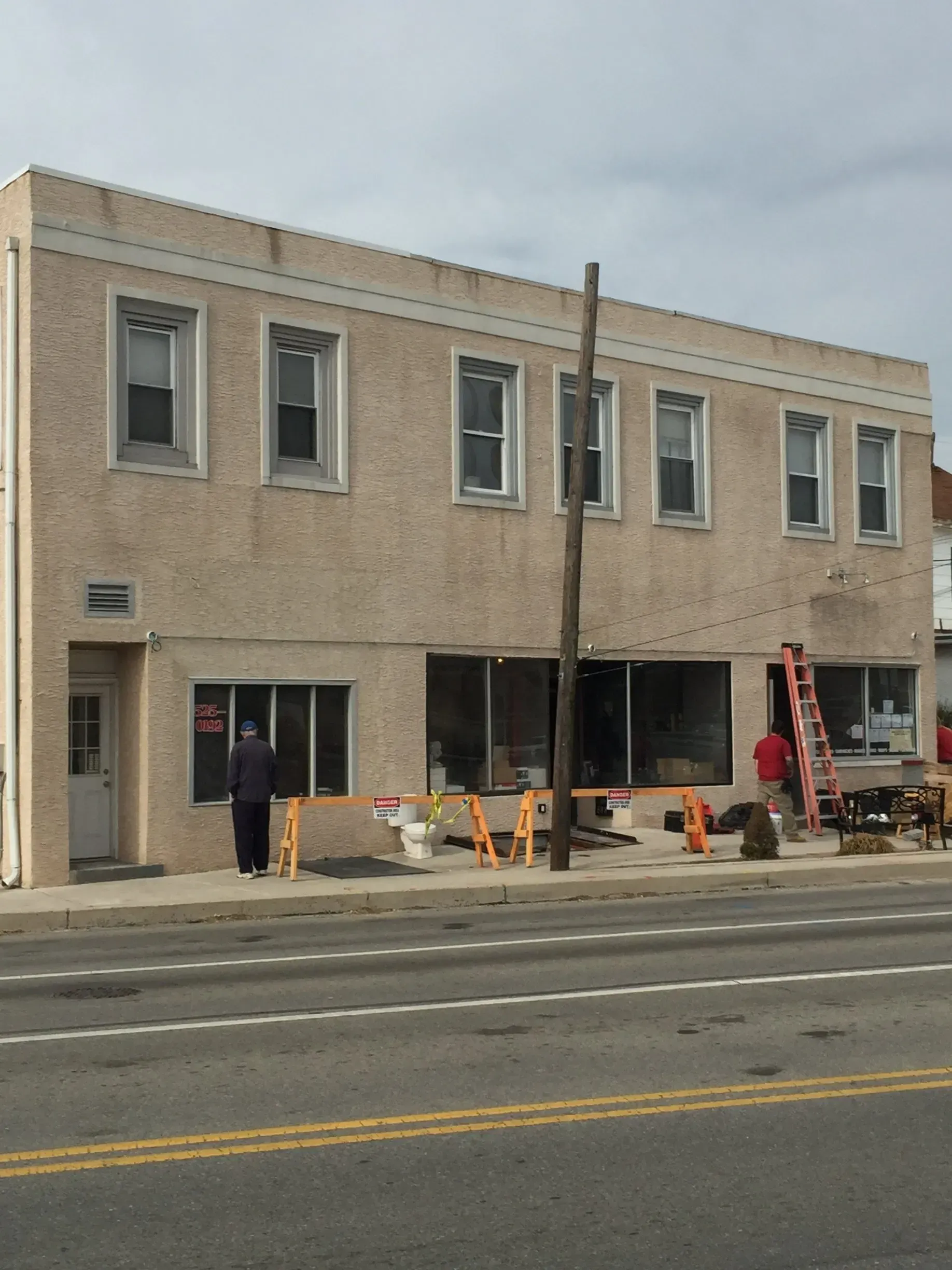 Brick storefront under renovation with workers, orange cones, and scaffolding along a street