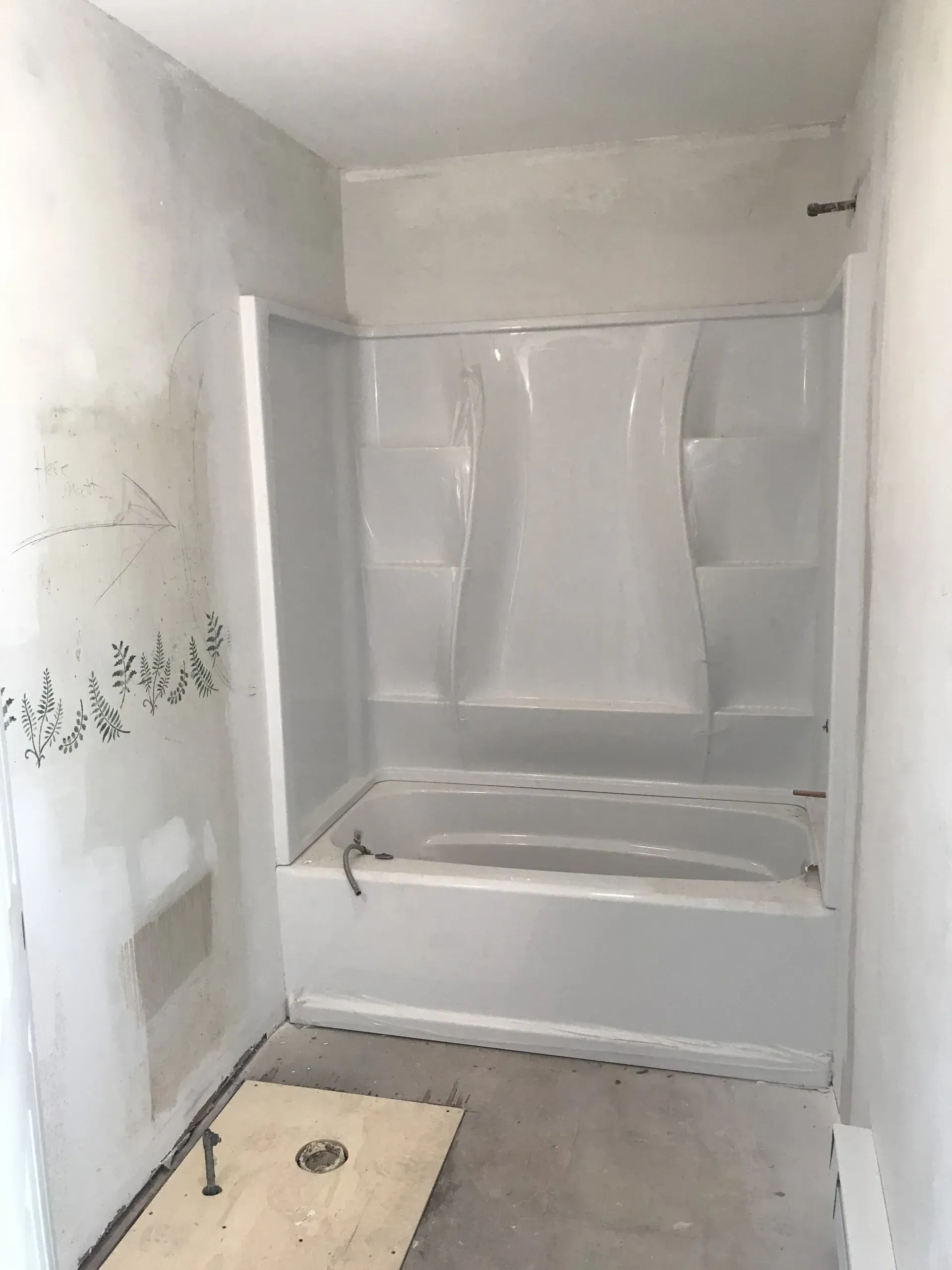 Small bathroom under renovation with a bathtub/shower, exposed drywall, and a bare concrete floor.
